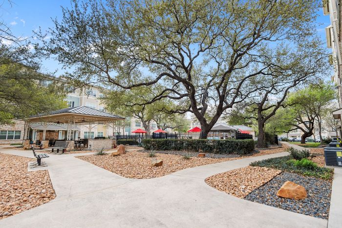 Serene apartment courtyard with lush trees, modern gazebo, and inviting seating areas.