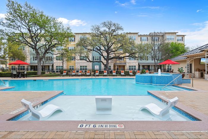 Luxurious apartment complex with a sparkling pool, relaxing lounge chairs, and vibrant red umbrellas for a resort-style experience.
