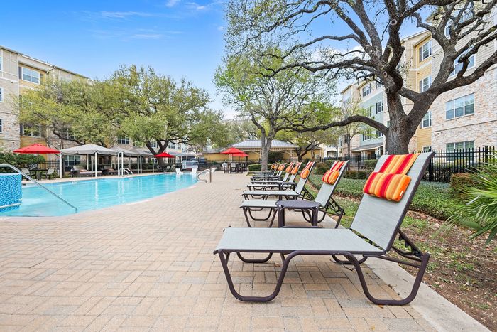 Luxurious apartment complex pool area with inviting lounge chairs and vibrant umbrellas set among lush greenery, offering a serene relaxation space.