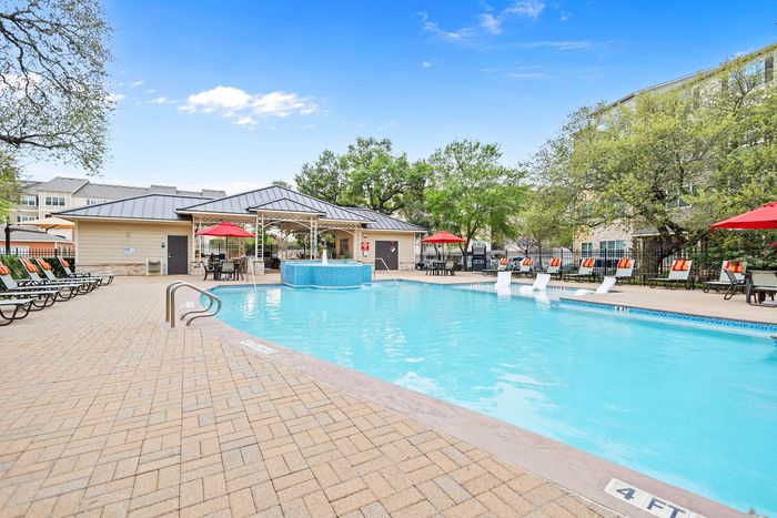 Inviting apartment complex pool with lounge chairs, vibrant red umbrellas, and a spacious seating area under a stylish gazebo.