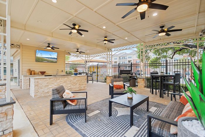 Chic outdoor lounge with modern wicker furniture, stylish ceiling fans, and a built-in stone bar, perfect for entertaining.