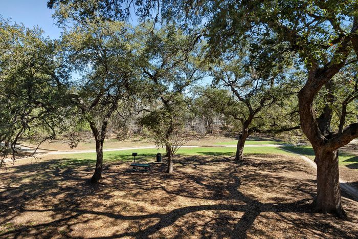 Serene apartment view featuring lush trees, a picnic area, and winding pathways under a clear blue sky.