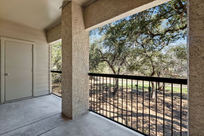 Inviting balcony view with textured walls overlooking a serene park with lush greenery.
