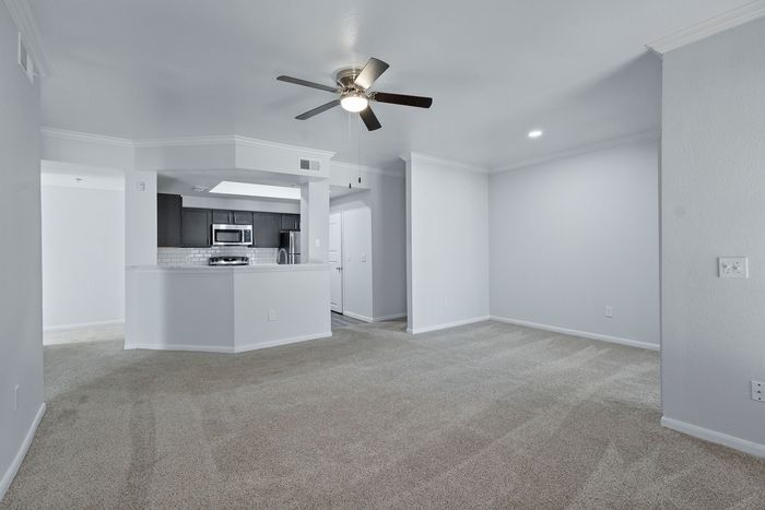 Elegant open-concept living space featuring plush carpet, a gourmet kitchen with modern stainless steel appliances, and stylish ceiling fan lighting.