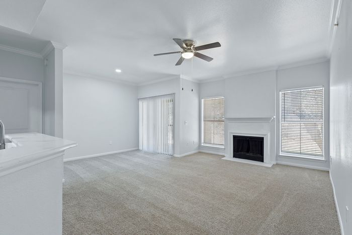 Bright, spacious living room with plush carpeting, large windows, and a cozy fireplace, perfect for relaxation and entertaining.