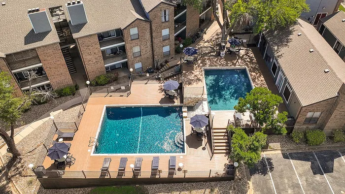 Aerial view of a stylish apartment complex featuring two sparkling swimming pools, surrounded by inviting sun loungers and shaded seating areas.