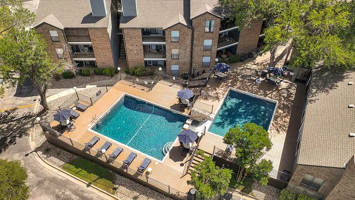 Luxurious aerial view of a modern apartment complex featuring two sparkling swimming pools surrounded by elegant decking and lush greenery, offering a perfect retreat for relaxation and leisure.