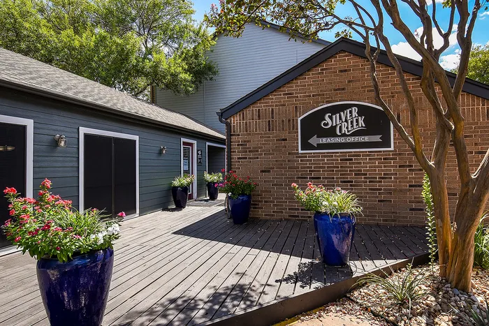 Inviting Silver Creek leasing office exterior with vibrant blue planters and lush greenery on a sunny day.