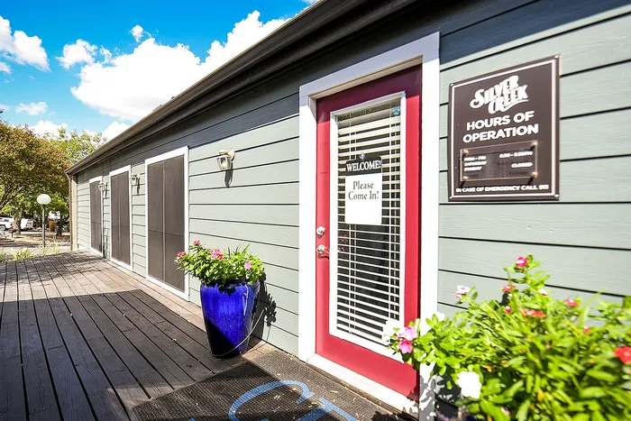 Inviting exterior of Silver Creek with charming red door, lush green planters, and a welcoming atmosphere under a vibrant blue sky.
