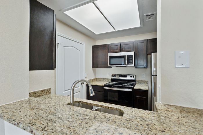 Modern kitchen with elegant granite countertops, sleek stainless steel fixtures, and dark wood cabinetry, offering a stylish cooking space.