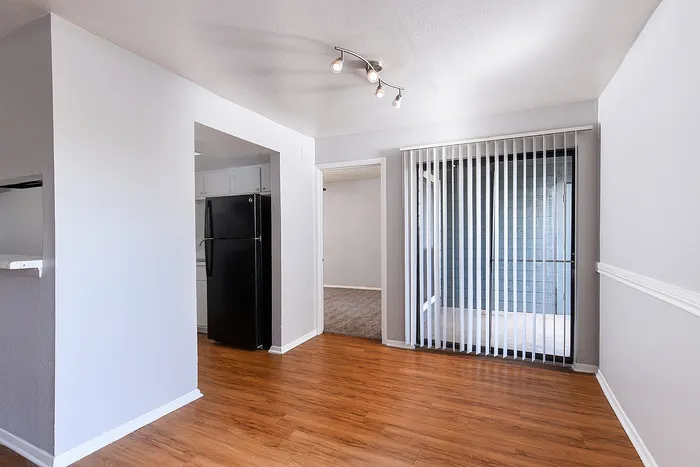 Bright apartment interior with sleek wood flooring, modern kitchen with black appliances, and large glass doors leading to a private balcony.