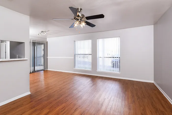 Spacious living room with elegant hardwood floors, large windows, and modern ceiling fan, perfect for natural light and comfort.