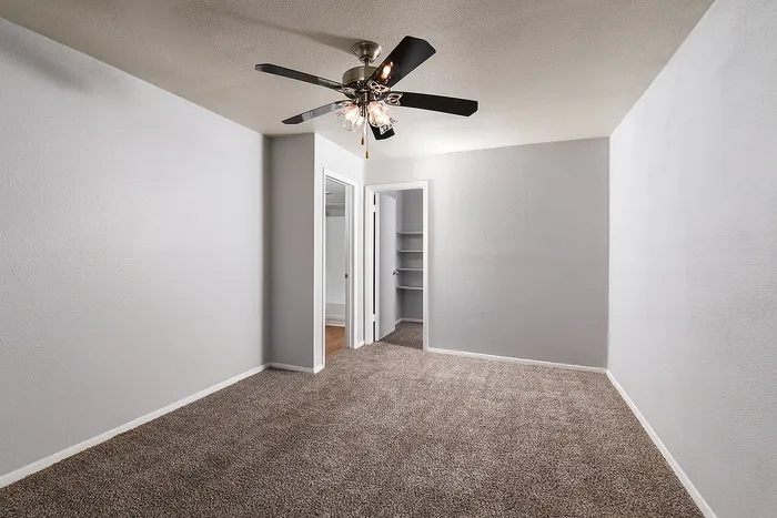 Bright and airy room with plush carpet and modern ceiling fan, leading to a generously sized closet and bathroom.