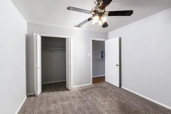 Bright bedroom featuring plush carpet, ample closet space, and a stylish ceiling fan.