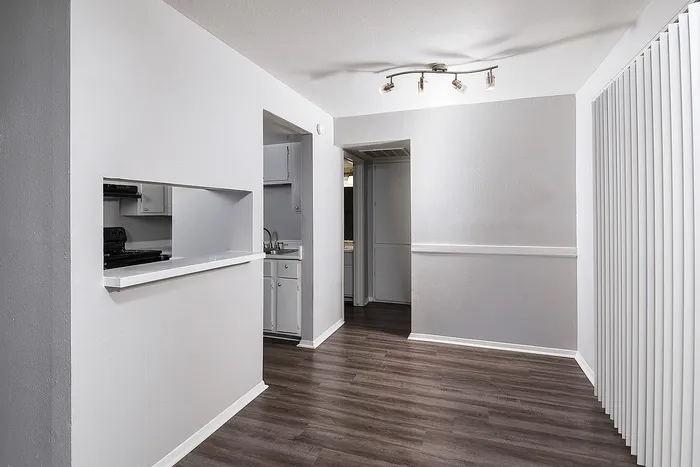 Modern apartment hallway with sleek hardwood floors, contemporary light fixture, and a view into a stylish kitchen with open shelving.