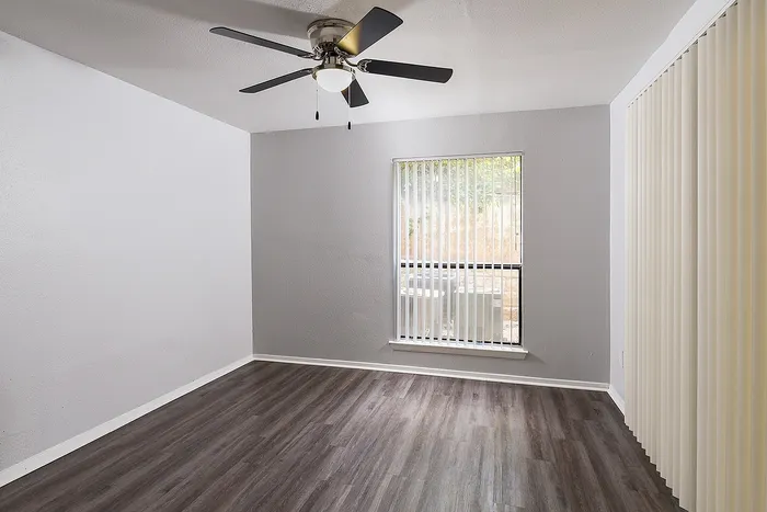 Bright and airy room featuring elegant wooden flooring, a modern ceiling fan, and large window with vertical blinds.