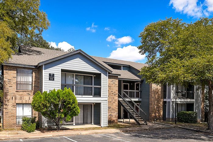 Charming two-story apartment building nestled among lush trees, featuring a stylish exterior with spacious balconies and a welcoming entrance.