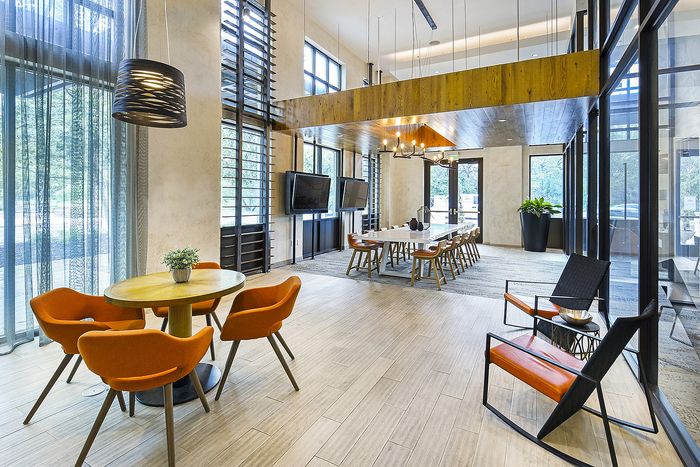 Spacious and modern communal area with stylish orange chairs, elegant lighting fixtures, and large windows for abundant natural light.