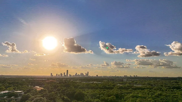 Breathtaking view of a city skyline at sunset, with a clear blue sky and scattered clouds, overlooking lush greenery.