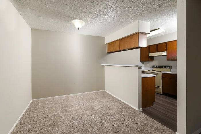 Cozy open-plan living and kitchen space with warm wooden cabinetry and soft carpeting, perfect for intimate gatherings.