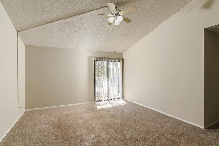 Bright living room with plush carpet, ceiling fan, and sliding glass doors leading to a patio.