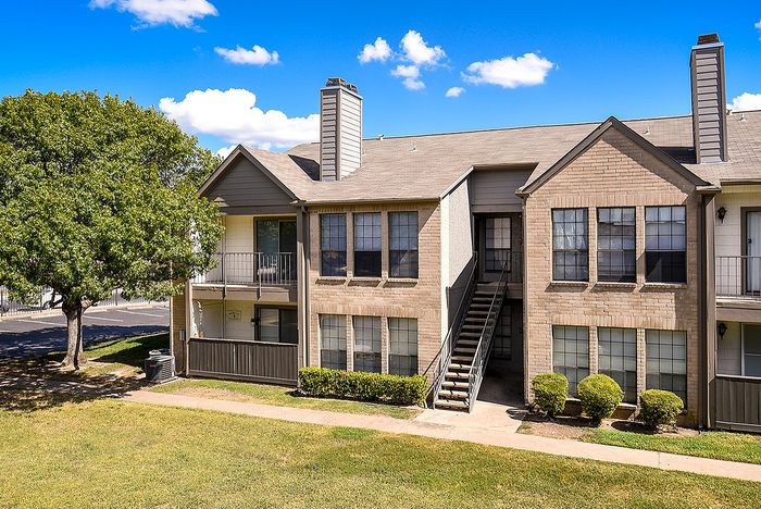 Charming brick apartment complex with inviting balconies and lush greenery under a bright blue sky.