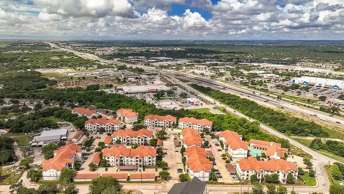 Charming aerial view of a vibrant apartment community with picturesque red rooftops, nestled amid lush greenery and a sprawling urban landscape.