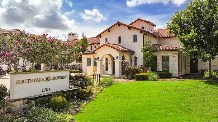 Charming Southpark Crossing entrance surrounded by lush greenery and vibrant flowers, showcasing elegant architecture under a clear blue sky.