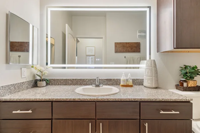 Modern bathroom vanity with granite countertop, illuminated mirror, and chic decor accents.