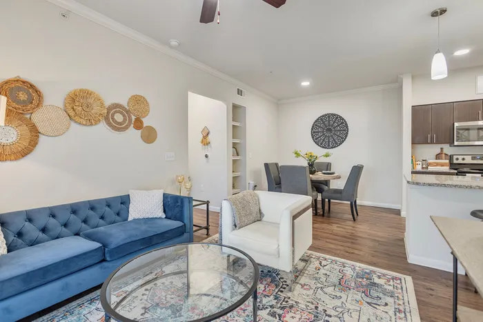 Chic open-plan living room featuring a plush blue sofa, elegant accent chair, and stylish dining area adjacent to a modern kitchen.