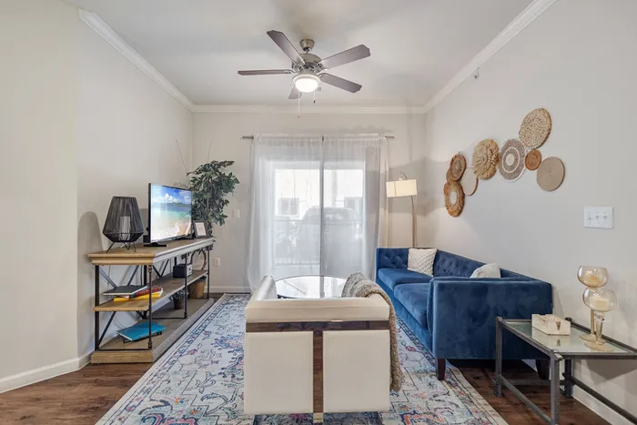 Charming living room featuring a cozy blue sofa, elegant decorative wall accents, stylish ceiling fan, and natural light filtering through sheer curtains.