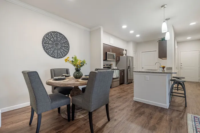 Chic open-concept dining and kitchen area with modern decor, featuring a stylish round table, plush seating, and a sleek kitchen island with bar stools.