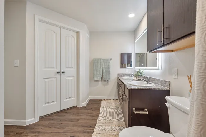 Elegant and spacious bathroom featuring double sinks, modern cabinetry, and stylish fixtures with warm wood flooring.