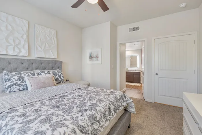 Bright and elegant bedroom with plush bedding, modern decor, and an en-suite bathroom with sleek cabinetry.