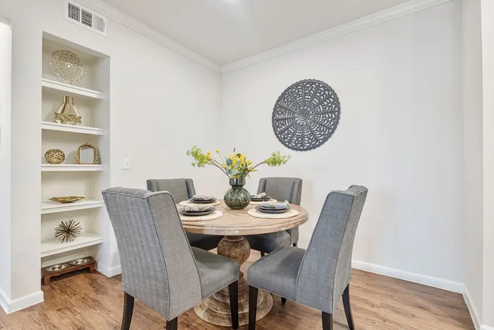 Elegant dining area with cozy round table, stylish gray chairs, and vibrant floral centerpiece, accented by chic wall decor and artistic shelving.
