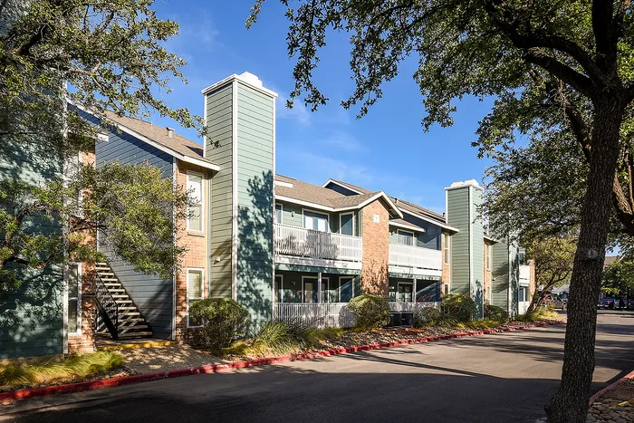Charming apartment building with modern architecture nestled among lush trees and vibrant greenery on a sunny day.