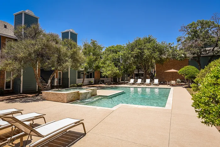 Luxurious apartment complex featuring a serene outdoor pool area with sun loungers, surrounded by lush greenery and modern architecture.