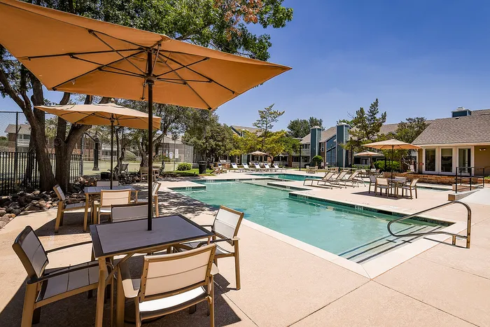 Inviting outdoor pool area with stylish seating and umbrellas, surrounded by lush greenery and modern architecture under a clear blue sky.
