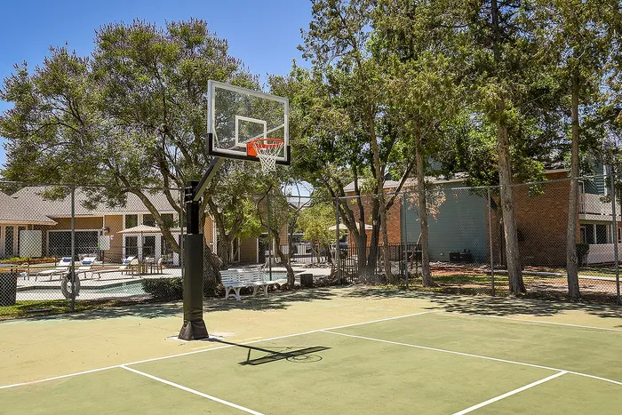 Inviting outdoor basketball court surrounded by lush trees and modern residential buildings in a vibrant community setting.