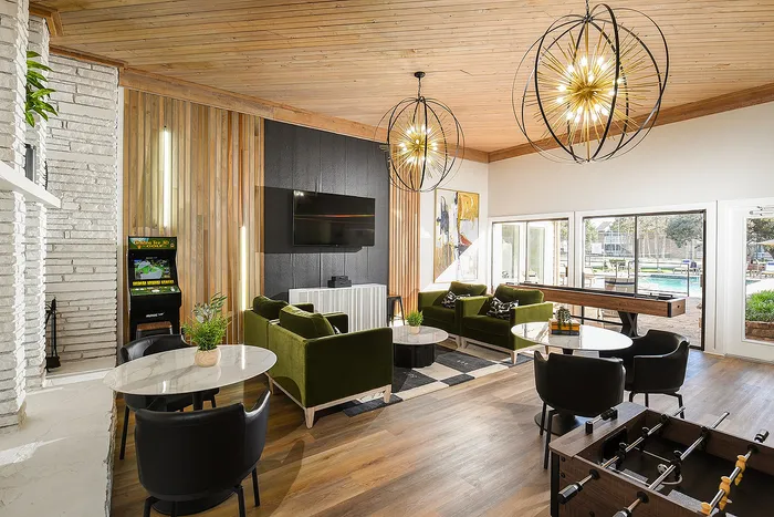 Chic lounge area featuring plush green sofas, modern lighting fixtures, and a pool view, perfect for relaxation and entertainment.