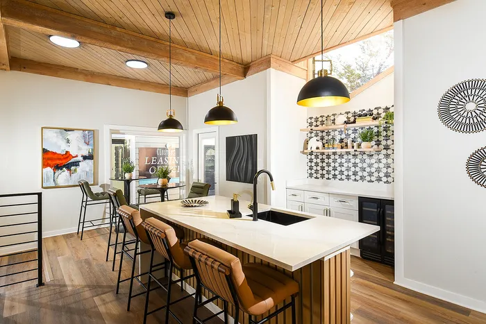 Modern kitchen with stylish pendant lighting, sleek countertops, and elegant bar stools, featuring open shelves with chic decor and a vibrant art piece.