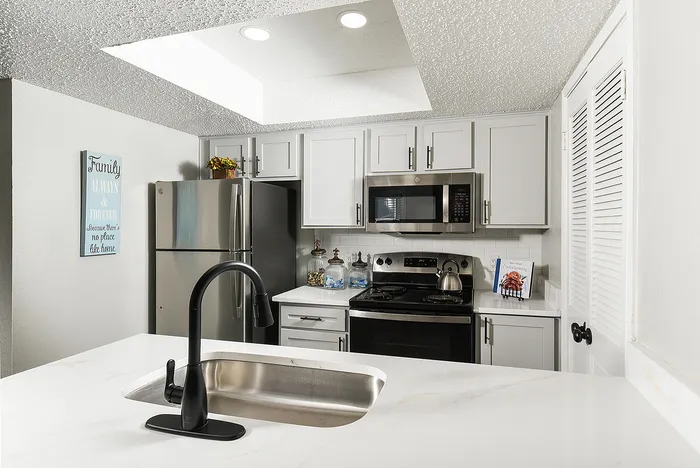 Modern kitchen with sleek stainless steel appliances, elegant white cabinetry, and a stylish black faucet over a marble countertop.