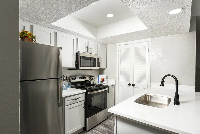 Modern kitchen design with stainless steel appliances, sleek white cabinetry, and elegant marble countertops, bathed in natural light.