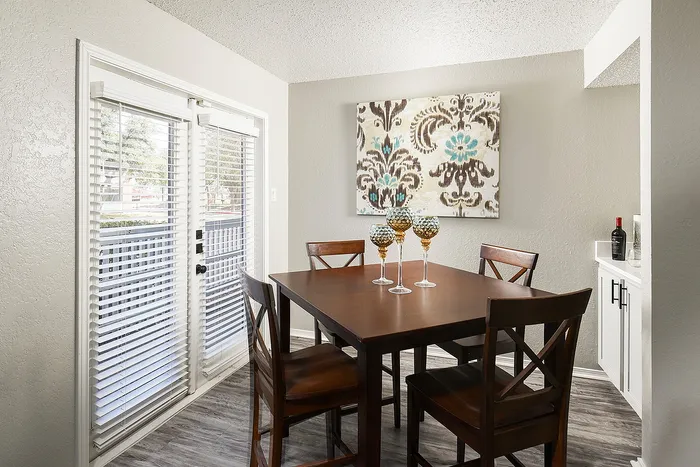 Inviting dining area with elegant wooden table and chairs, adorned with stylish glassware, set against a background of modern art and natural light from large windows.