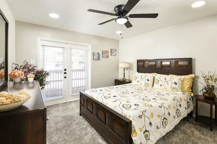 Charming bedroom with elegant floral bedding, dark wood furniture, and bright natural light streaming through double glass doors.