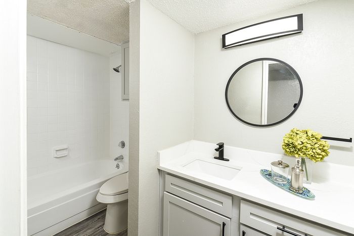 Bright and modern bathroom featuring a sleek vanity with black fixtures, a round mirror, and elegant floral decor.