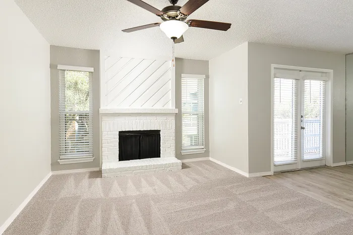 Bright living room with elegant white brick fireplace, plush carpet, and French doors opening to a sunlit outdoor deck.