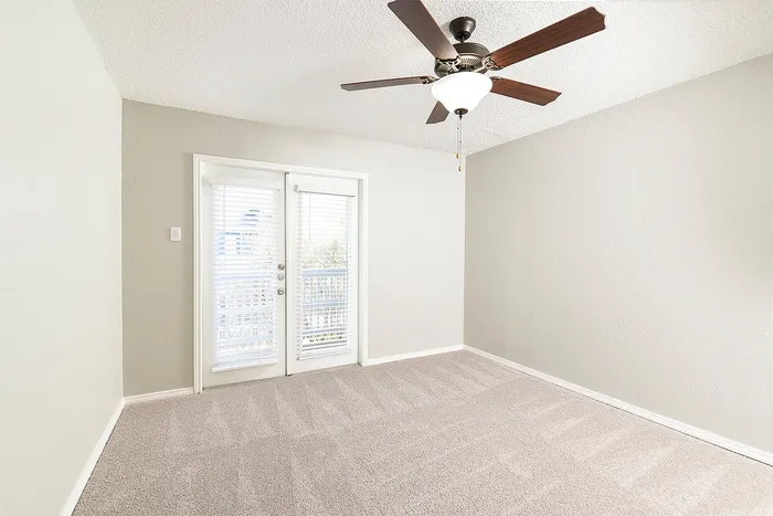 Bright and airy room with plush carpeting, stylish ceiling fan, and elegant French doors opening to a balcony.