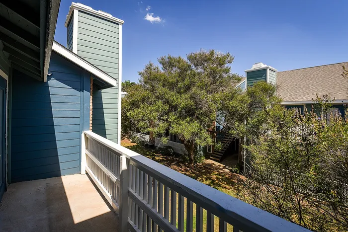 Charming apartment balcony with a serene view of lush greenery and modern architecture against a clear blue sky.