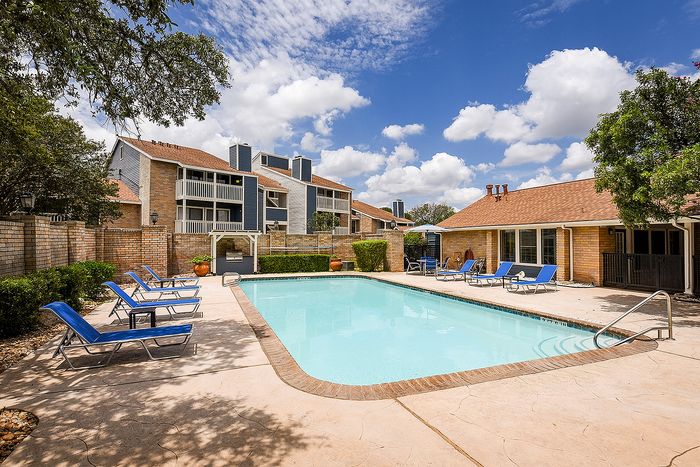 Charming apartment complex featuring a pristine swimming pool surrounded by inviting lounge chairs and lush greenery.
